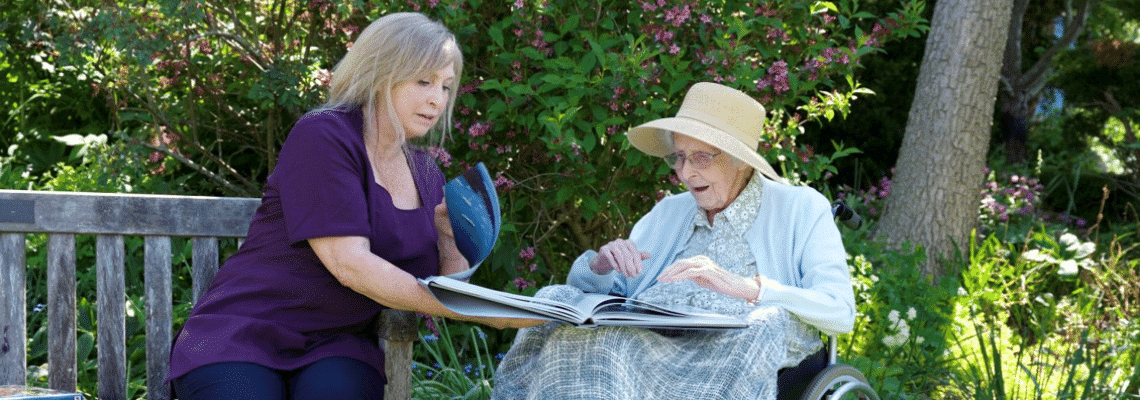 Nurse and resident in gardens of nursing home looking through book.
