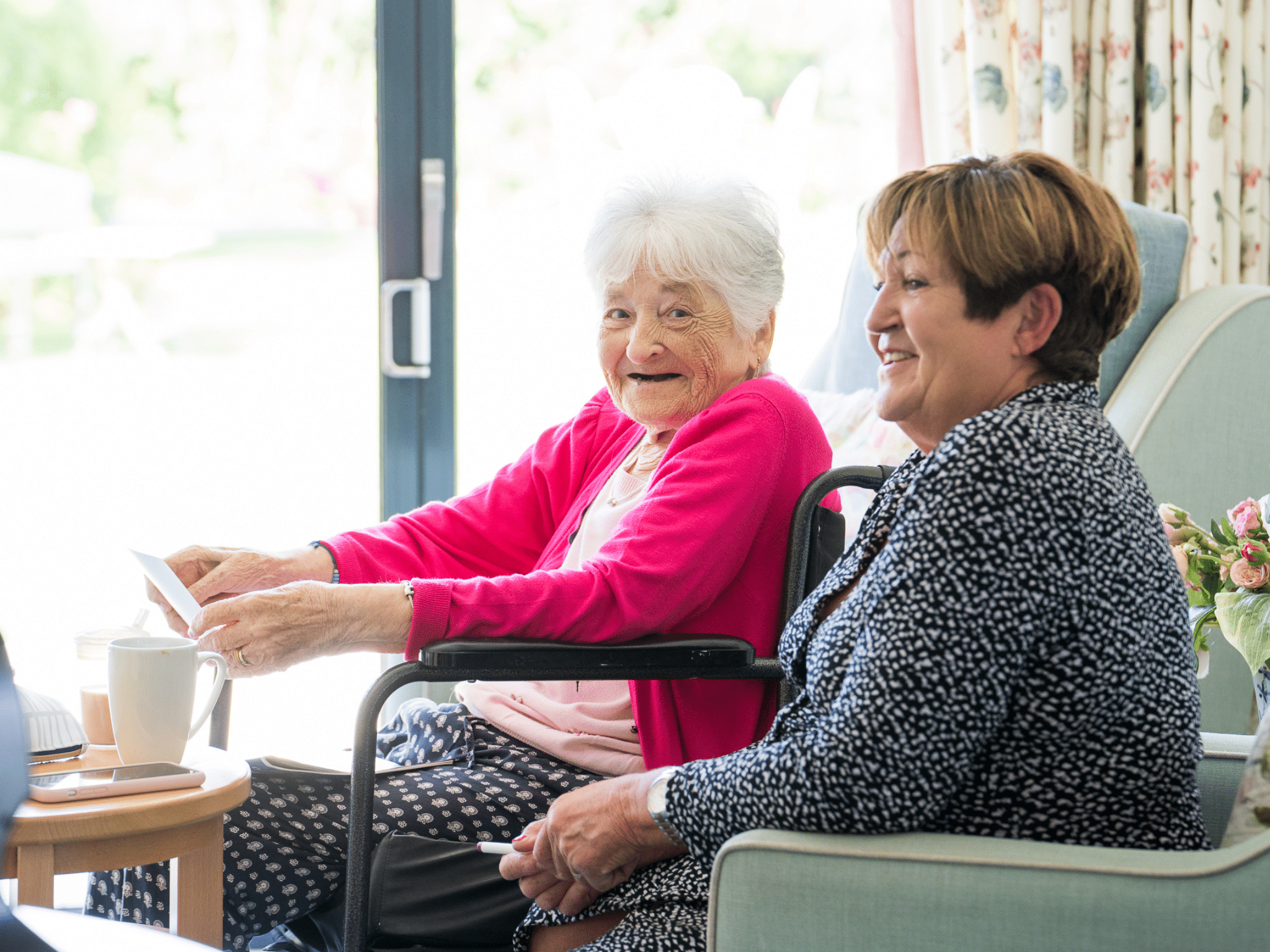 A daughter settling in your elderly mother into a care home, they are happy and smiling.