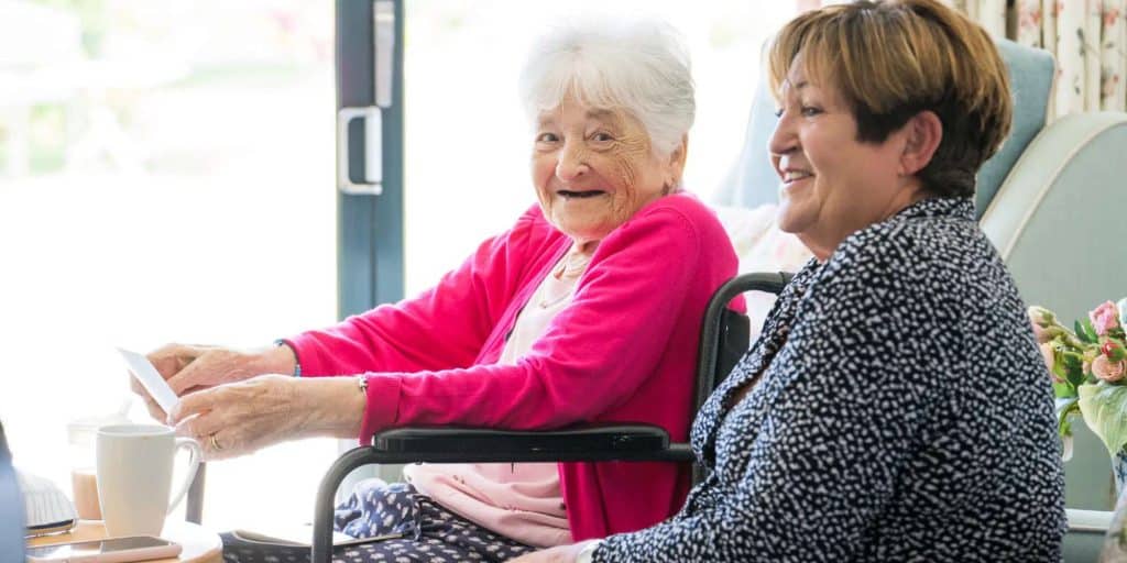 A daughter settling in your elderly mother into a care home, they are happy and smiling.