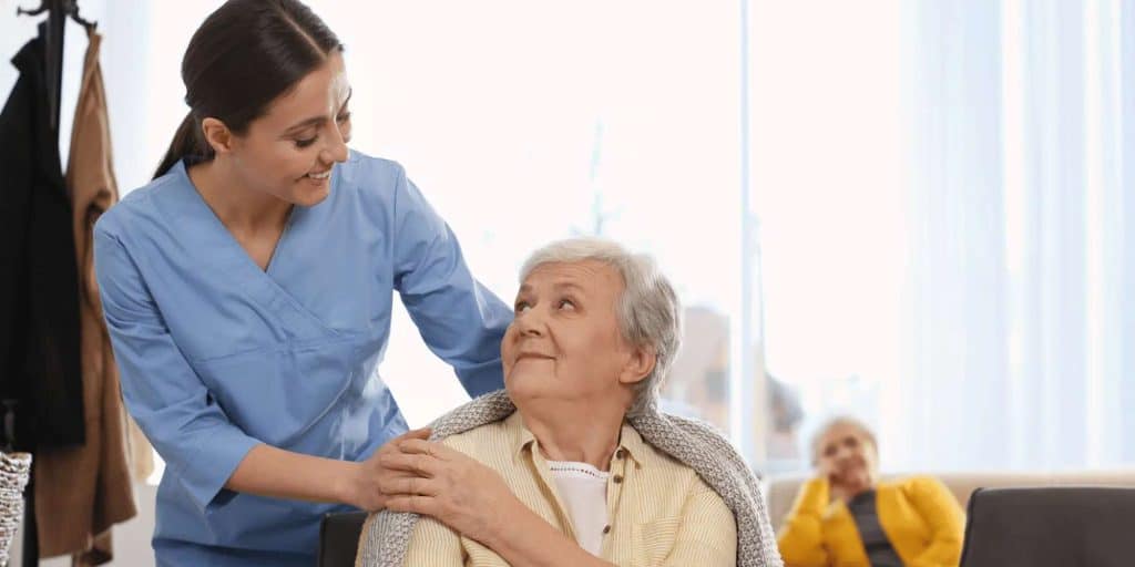 Nurse wrapping blanket over elder lady's shoulder smiling